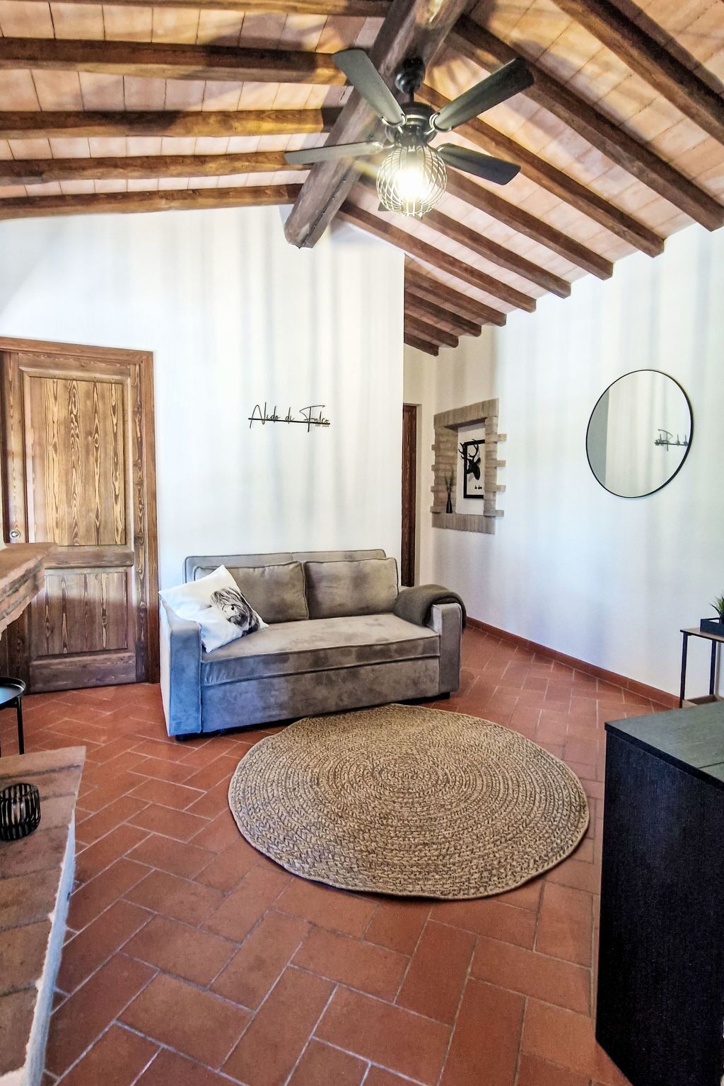 Un salon chaleureux avec un plafond en bois, un canapé gris, un tapis rond en fibres naturelles et une porte en bois.