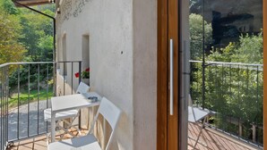 Ein Balkon mit Tisch und Stühlen, eine hölzerne Pergola und Blick auf Grünflächen.