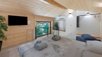 A modern bedroom with a wooden ceiling, a flat-screen TV, a balcony with a view, and a bed with rolled towels.