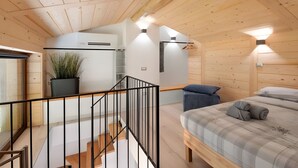 Ein Holzhütten-Innenraum mit Treppe, einem Bett, einer kleinen Küche und einem Blumentopf.