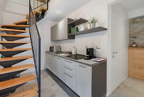 A modern kitchen with a wooden staircase, built-in cabinets, a coffee machine, and a stone accent wall.