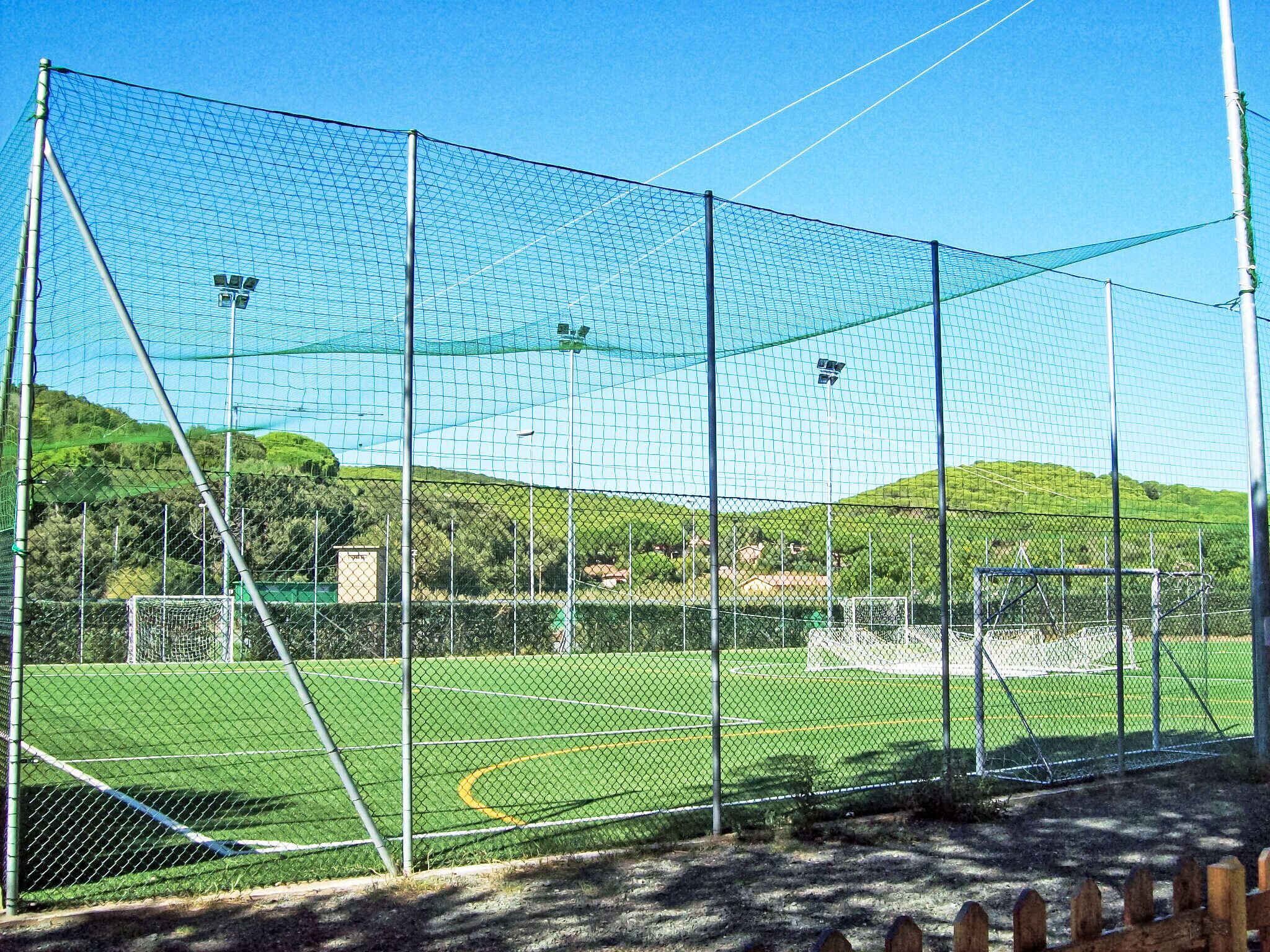 Um campo esportivo cercado por uma grade de arame, com traves e refletores.
