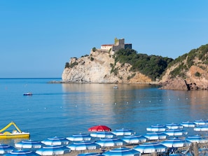 A coastal scene with a historic building on a cliff, calm sea, and beach umbrellas. - Prestige Family by Interhome (Castiglione della Pescaia)