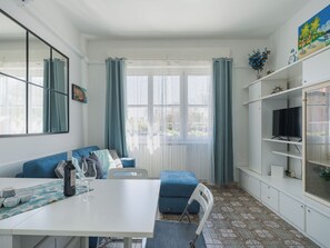 Ett modernt vardagsrum med ett vitt bord, en blå soffa och en tv som står på en hylla.
