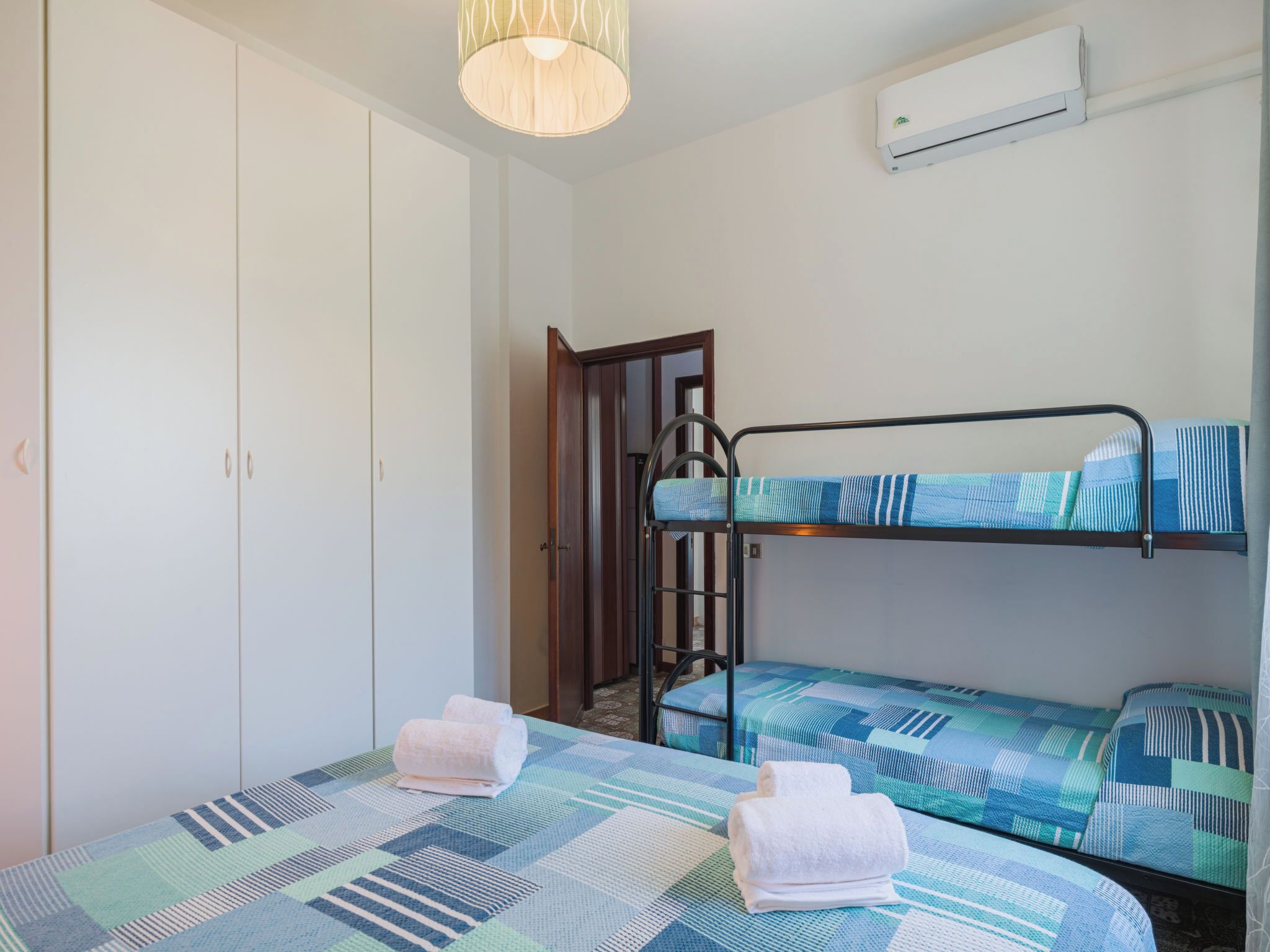 A room with bunk beds, a wardrobe, a hanging light fixture, and an air conditioning unit.