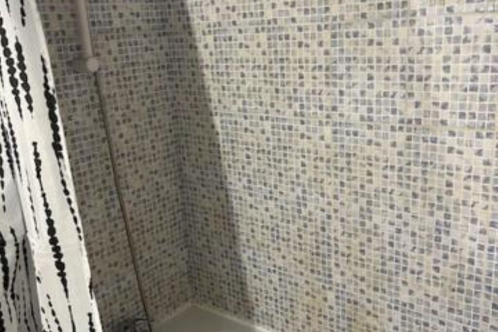 A bathroom with mosaic tile walls and a white shower curtain.