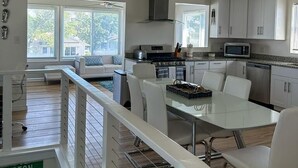 A modern kitchen with white cabinets, a dining table, and chairs. - 4BR Home Near the Beach! | Canal Access + Porch (South Bethany)