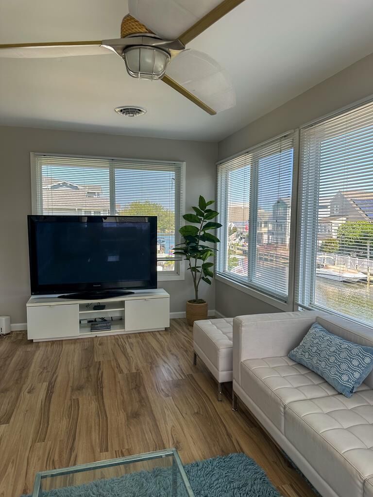A living room with a flat-screen TV, white sofa, and large windows.