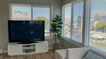 A living room with a flat-screen TV, white sofa, and large windows.