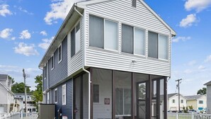 A two-story house with a covered porch, a fenced yard, and a clear blue sky. - 4BR Home Near the Beach! | Canal Access + Porch (South Bethany)