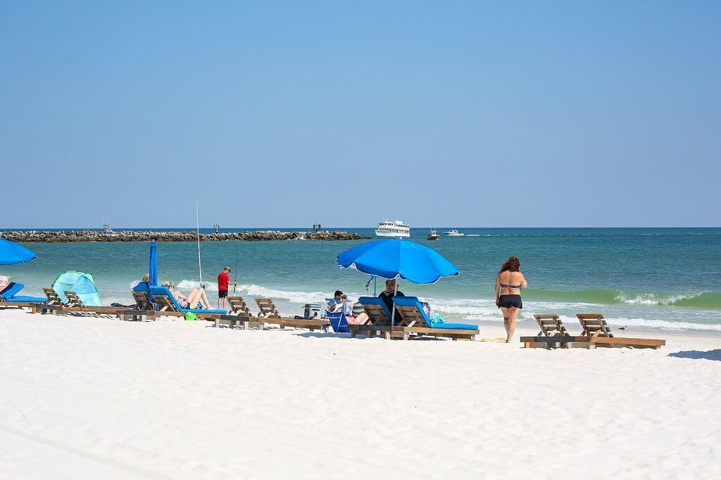 A beach with sun loungers and umbrellas, a pier in the background, and a clear sky.