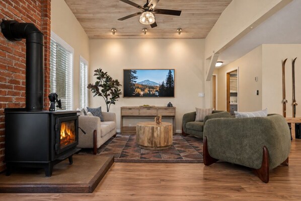 A cozy living room with a fireplace, comfortable seating, a wooden coffee table, and a painting on the wall. - Private Sauna + Hot Tub - Mins to Mt. Bachelor (Bend)