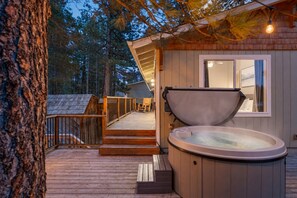 Une terrasse en bois mène à un espace équipé d’un bain à remous, avec une fenêtre donnant sur un paysage boisé.