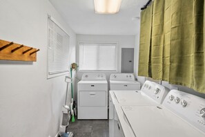 Une buanderie équipée de deux machines à laver, d’un sèche-linge et d’un balai.