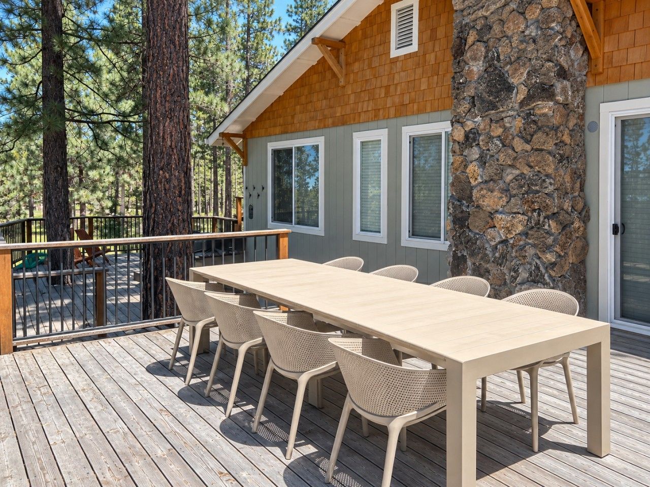 A wooden deck with a table and chairs, a stone pillar, and a view of trees.