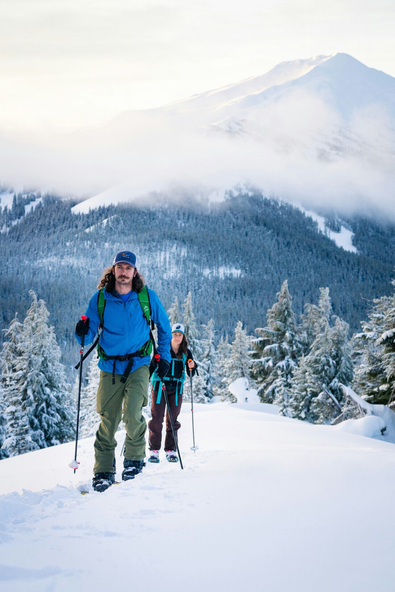 A snowy mountain landscape with two people hiking.