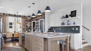 Eine moderne Küche mit einer zentralen Kochinsel, Pendelleuchten und einem Essbereich mit Stühlen und Tisch.