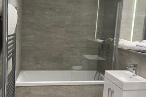 Een moderne badkamer met een douche in een glazen cabine, een witte badkuip en een wastafelmeubel.
