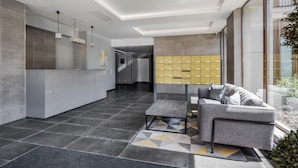 A modern lobby with a reception desk, a seating area with a sofa and armchairs, a geometric patterned rug, and a row of yellow lockers. - 1 Bed - Sleeps 2 - City Centre - Free Parking (St Albans)