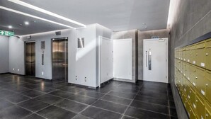 A modern elevator area with metallic elevators, a green exit sign, and a row of lockers on the right. - 1 Bed - Sleeps 2 - City Centre - Free Parking (St Albans)