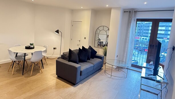 A modern living room with a grey sofa, a round dining table with chairs, a small potted plant, and a glass coffee table. - 1 Bed - Sleeps 2 - City Centre - Free Parking (St Albans)
