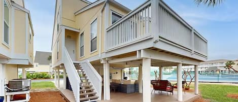 A two-story house with a covered deck, outdoor seating, and a staircase leading to the upper floor.