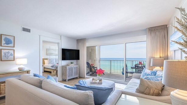 Un salon spacieux avec un grand canapé, une table basse et un téléviseur. Il y a un balcon avec vue sur l’océan.