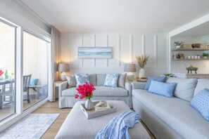 A modern living room with a sofa set, a coffee table with a vase of flowers, and a dining area with a table and chairs. - Beach House 601c- Beach Rest (Miramar Beach)