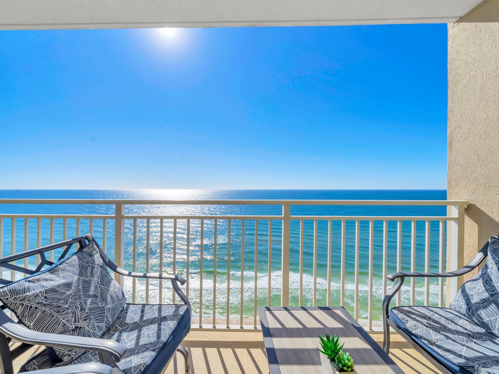 Un balcon avec deux chaises et une table, donnant sur une plage où l’on peut admirer les vagues et un ciel dégagé.