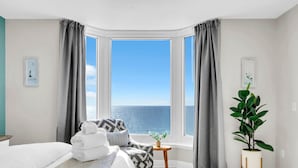 Hotellihuone, jossa on sänky, pieni pöytä, ruukkukasvi ja näkymä merelle.
