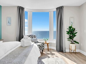 A hotel room with a bed, a small table, a potted plant, and a view of the sea. - Emerald Beach 1831 (Panama City Beach)