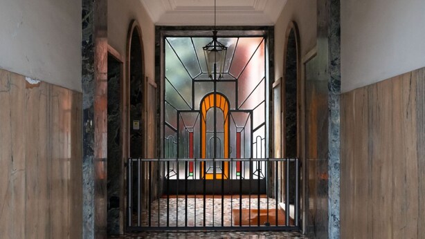 Un corridoio con pavimento piastrellato che conduce a una porta con una finestra a vetri colorati.