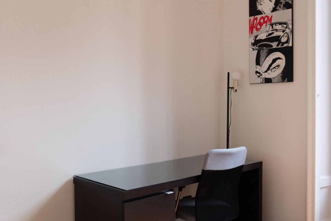 Un espacio de oficina moderno con un escritorio, una silla, un cartel en la pared y una lámpara de pie.