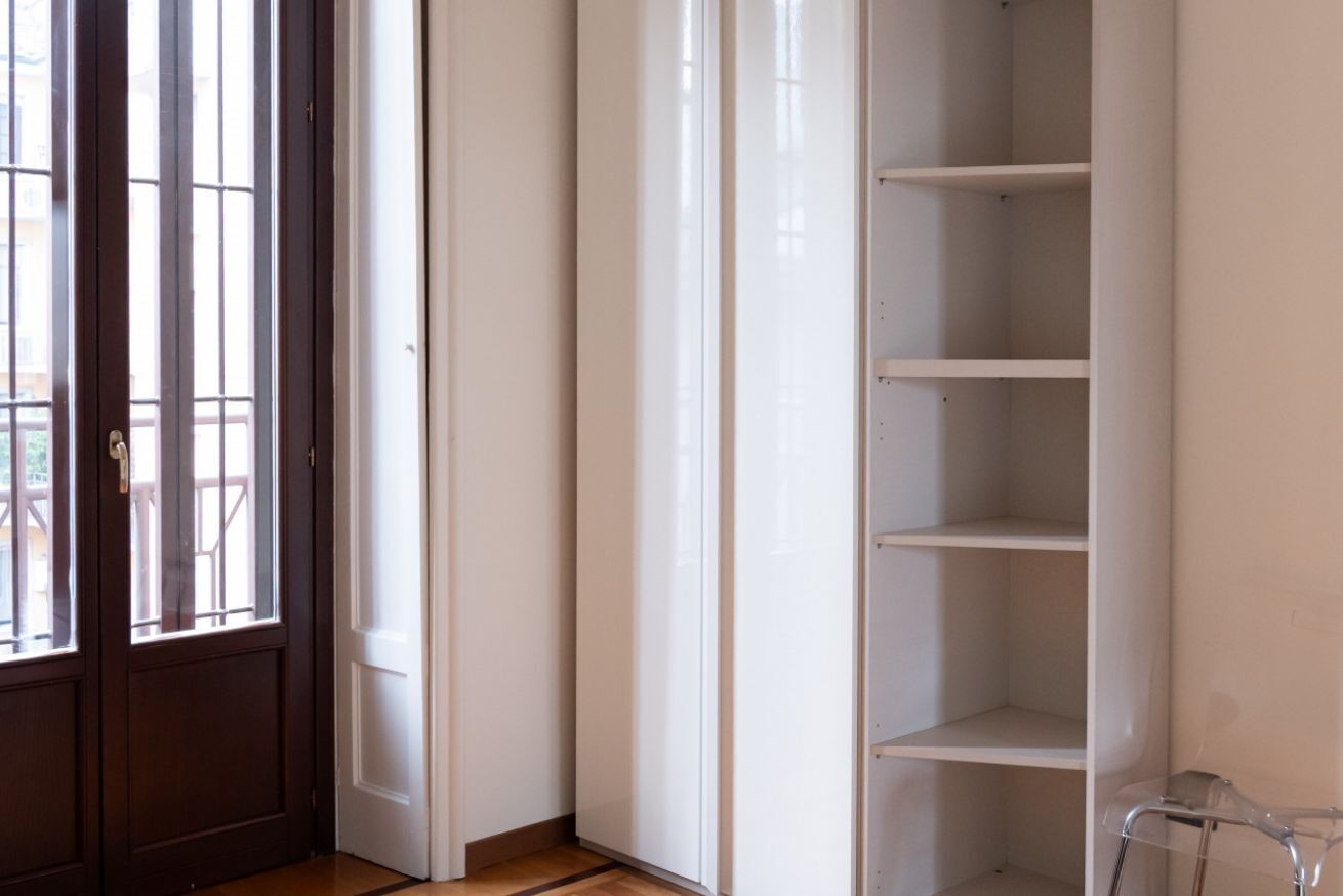 A room with a wooden door, a white wall, and a white shelving unit.
