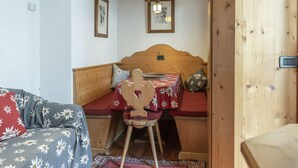 A cozy room with a wooden bed, a small table with a red tablecloth, and a wooden chair. - Casa Col 3, a charming two-room apartment (Cortina d´Ampezzo)