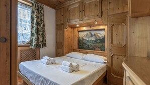 A wooden bedroom with a bed, pillows, and a painting of mountains. - Casa Col 3, a charming two-room apartment (Cortina d´Ampezzo)