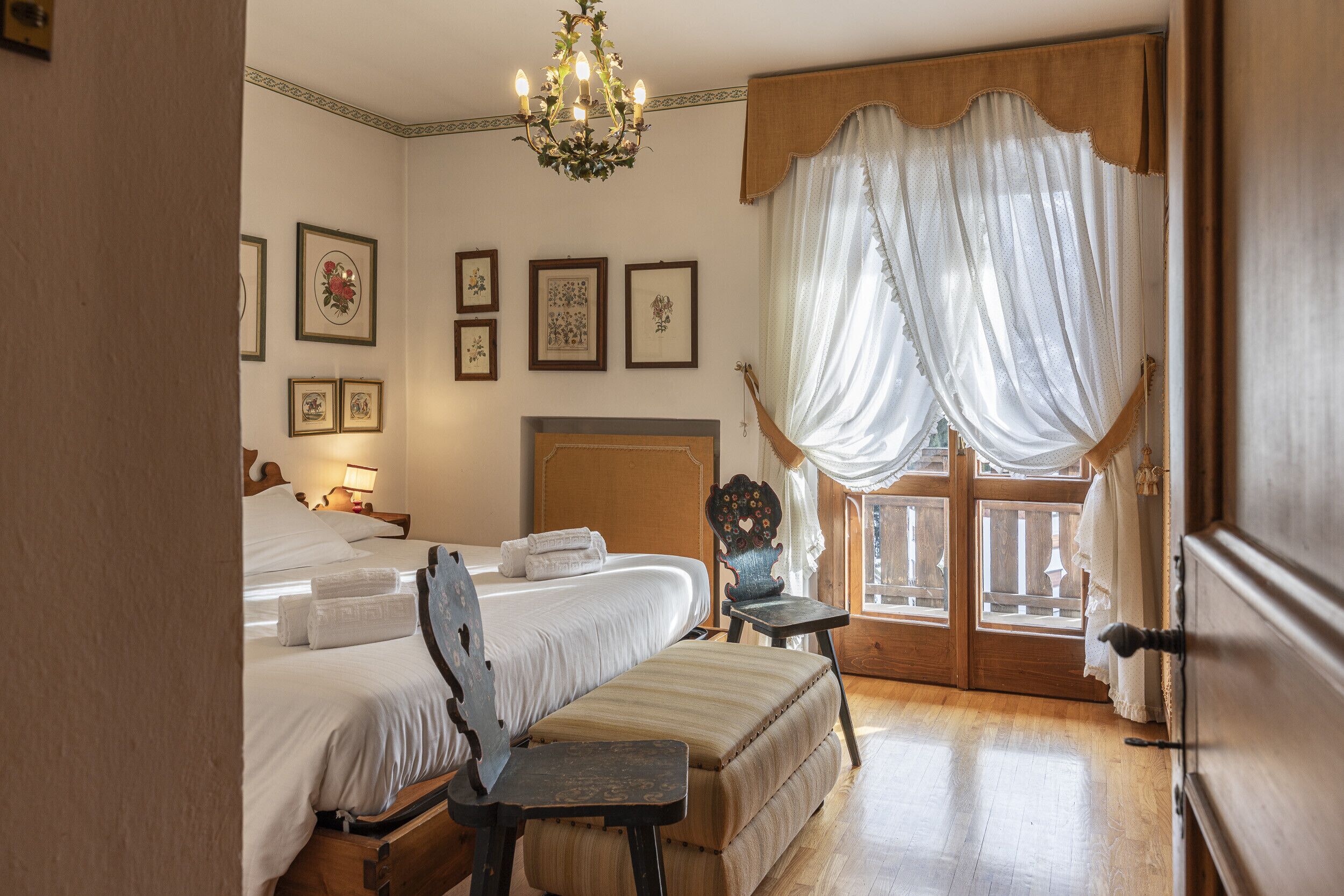 Una camera da letto con un letto grande, una sedia, pavimento in legno e una finestra con tende.