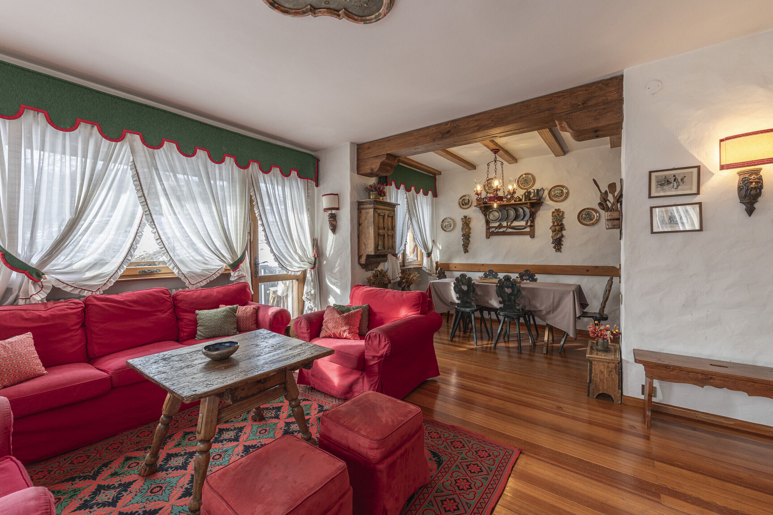 Un salon chaleureux avec un ensemble de canapés rouges, une table basse en bois et un tapis à motifs. On aperçoit à l’arrière-plan un coin repas avec une table et des chaises.