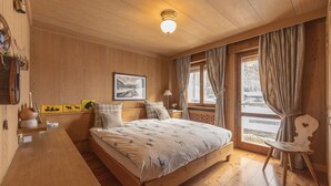 A wooden room with a bed, a nightstand, a lamp, and a window with curtains. - Casa Merisanda, comfortable and surrounded by Natur (Cortina d´Ampezzo)