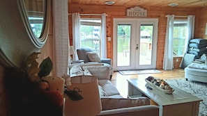 Una sala de estar acogedora con un sofá, una mesa de centro y una chimenea. Hay dos puertas que dan al exterior, y un letrero que dice 'Farm House'.