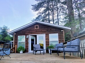 En træhytte med terrasse, to grå stole og et lille bord.