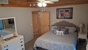 Une chambre à coucher avec un lit, une commode, un ventilateur de plafond, une porte et un tableau encadré au mur.