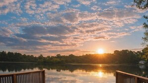 Une jetée en bois s’étendant sur un lac paisible, avec un coucher de soleil en arrière-plan.