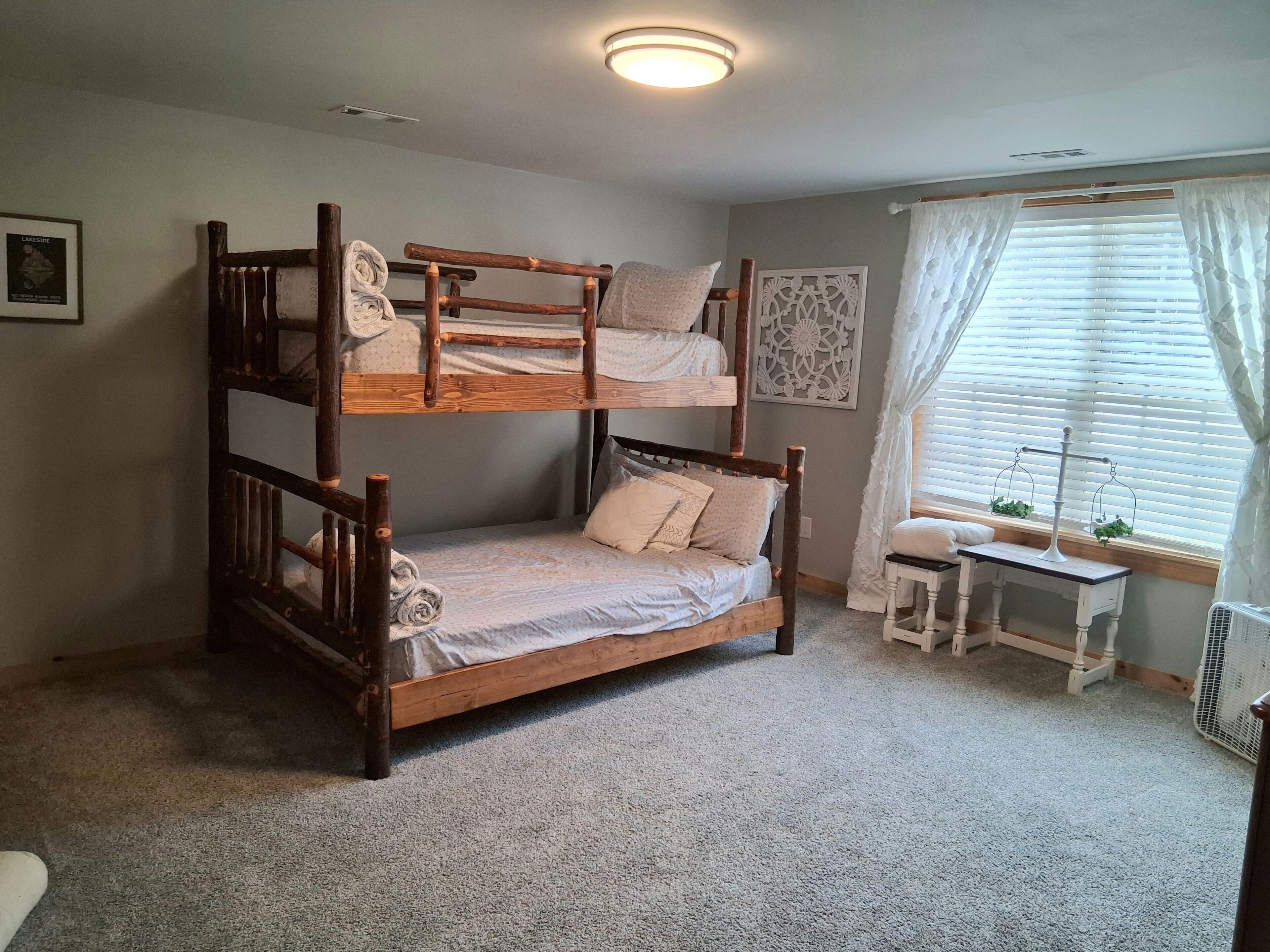 A bunk bed room with a small table and a window with curtains.