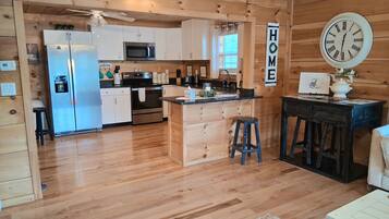 A wooden-paneled kitchen with a central island, a refrigerator, microwave, oven, and a clock on the wall.