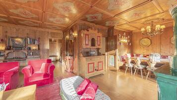 Un'ampia stanza con pannelli in legno, una zona pranzo con tavolo e sedie, e un'area salotto con poltrone imbottite rosse.