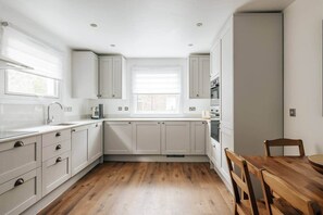 A kitchen with white cabinets, a wooden floor, and a window. - Modern 5-bed Home in Maida Vale (London)