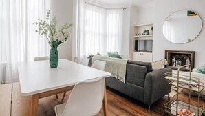 Moderni olohuone, jossa on valkoinen ruokapöytä, harmaa sohva ja TV-taso.