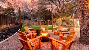 An outdoor seating area with wooden chairs and a fire pit, surrounded by trees and a wooden fence. - Ultimate Getaway • Pool • Game Room • Sleeps 12 (San Antonio)