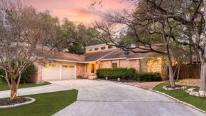 A two-story house with a brick exterior, a garage, and a well-maintained lawn. - Ultimate Getaway • Pool • Game Room • Sleeps 12 (San Antonio)